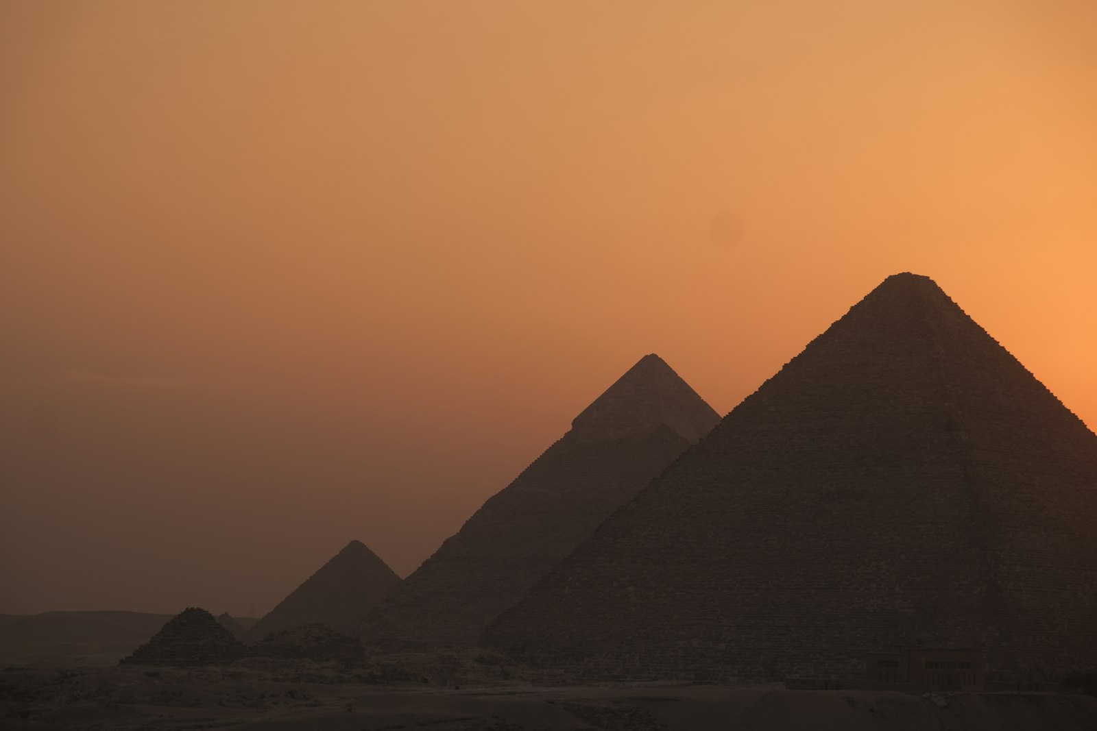 The pyramids of Giza silhouetted against a glowing orange sunset sky
